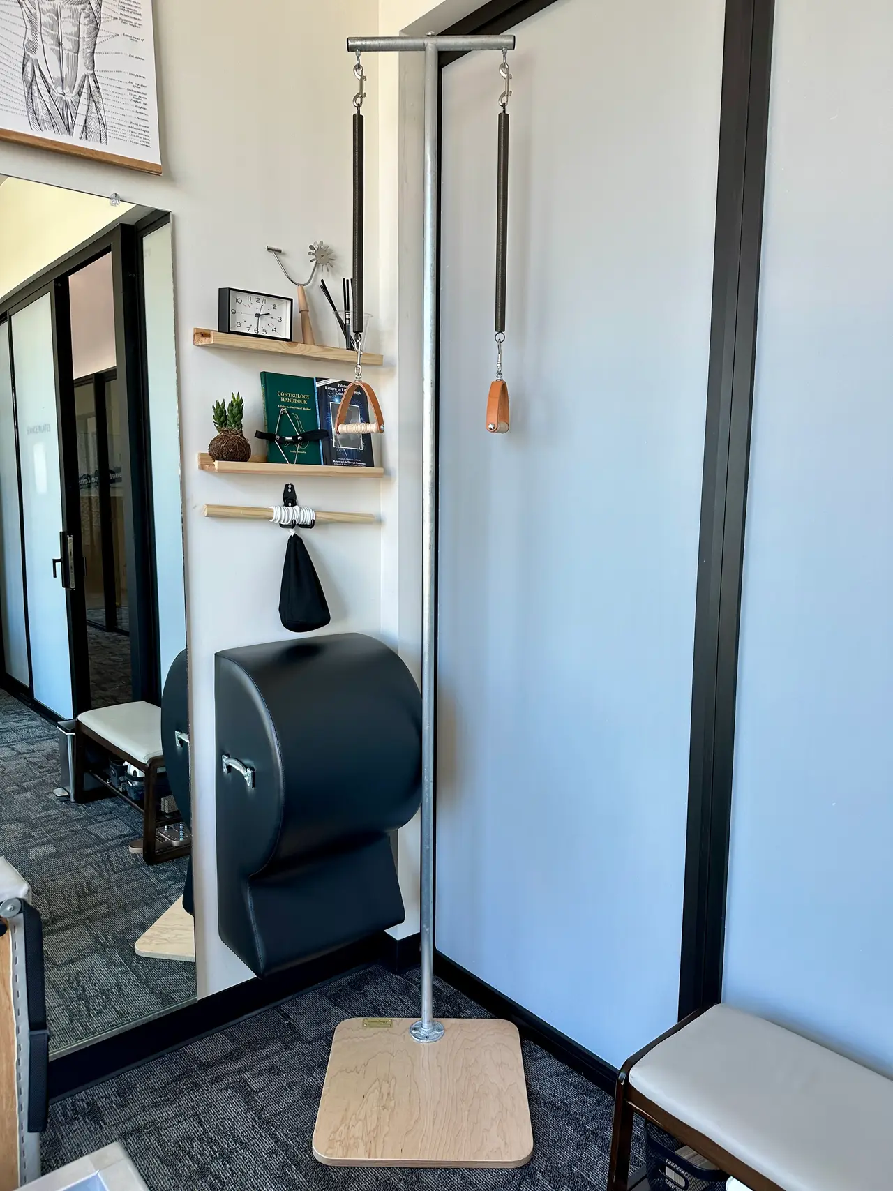 Classical Pilates Ped-o-Pull standing apparatus with leather handles beside a barrel reflected in the studio mirror