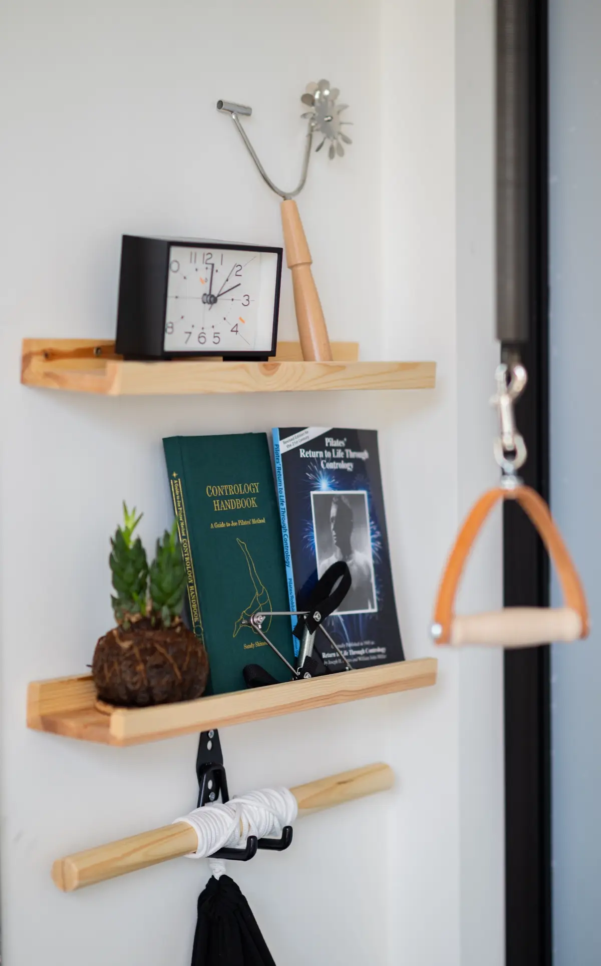 Studio shelf holding Joseph Pilates' Contrology Handbook and Return to Life Through Contrology beside a classical Pilates hand apparatus