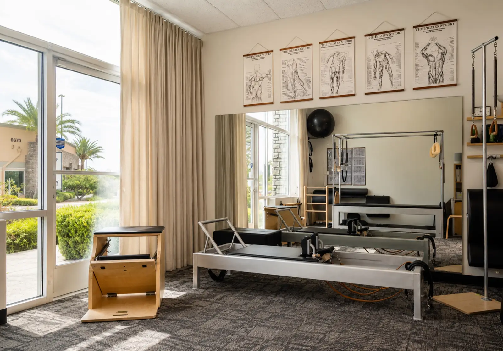 Classical Pilates studio in Southwest Las Vegas with Contrology Reformers and a Wunda Chair beneath framed anatomy charts, lit by floor-to-ceiling windows